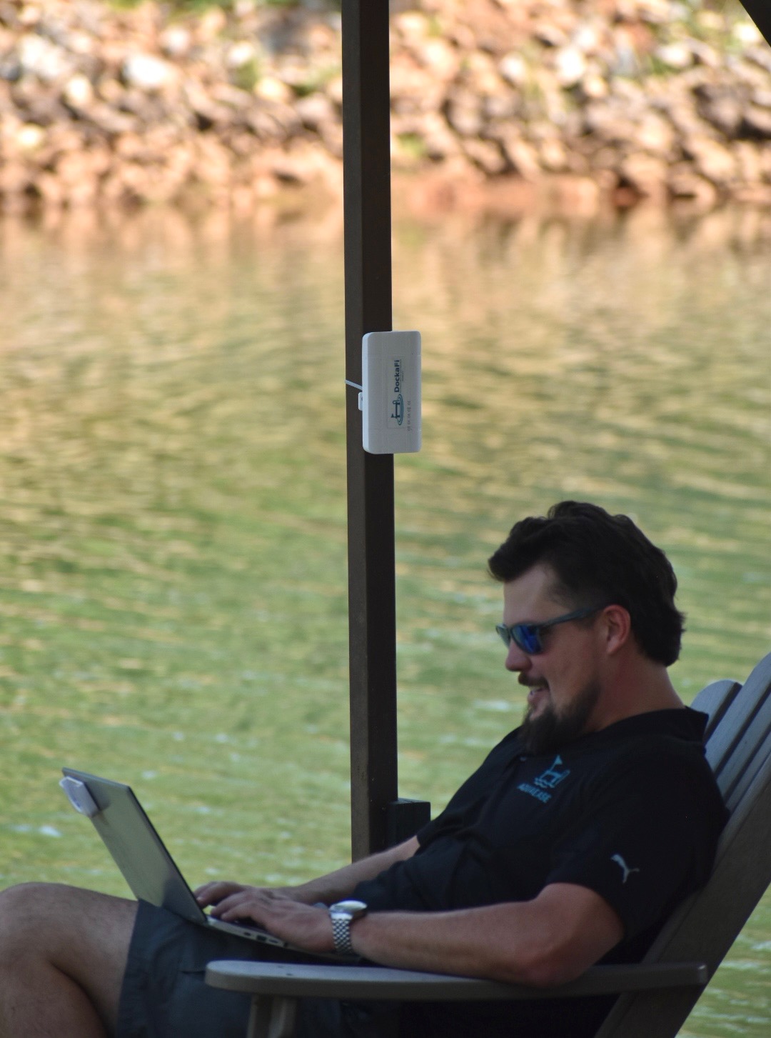 DockaFi mounted on dock post, user working on laptop at the water